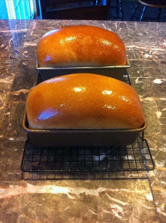 Delicious Freshly baked Amish white bread loaf with a golden-brown crust on a wooden cutting board.